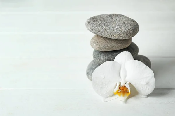 Стопка спа-камней и красивый цветок орхидеи на белом столе — стоковое фото