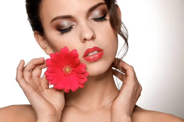 Porträtt av ung kvinna med vackra professionell makeup och blomma på ljus bakgrund — Stockfoto