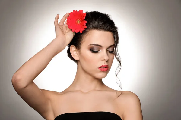 Retrato de jovem com bela maquiagem profissional e flor no fundo claro — Fotografia de Stock