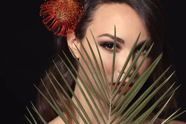 Portrait of young woman with beautiful professional makeup and palm leaf on dark background — Stock Photo, Image