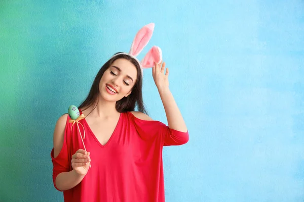 Mooie jonge vrouw met paasei en bunny oren op kleur achtergrond — Stockfoto