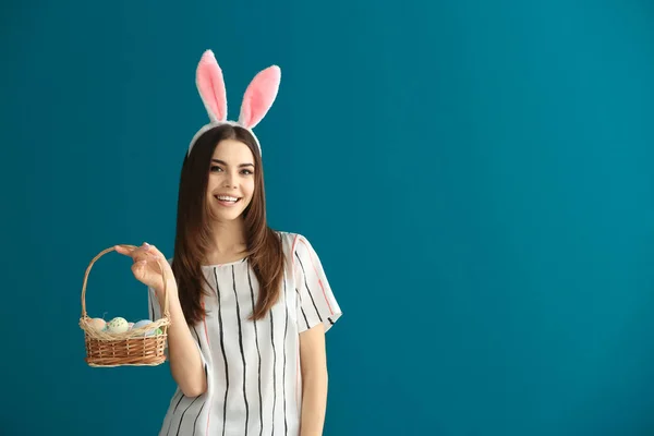 Bella giovane donna con uova di Pasqua e orecchie di coniglio su sfondo di colore — Foto Stock