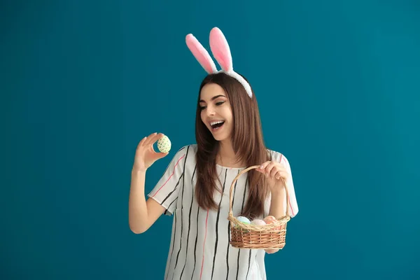 Beautiful young woman with Easter eggs and bunny ears on color background — Stock Photo, Image