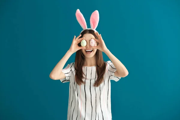 Mooie jonge vrouw met paaseieren en bunny oren op kleur achtergrond — Stockfoto