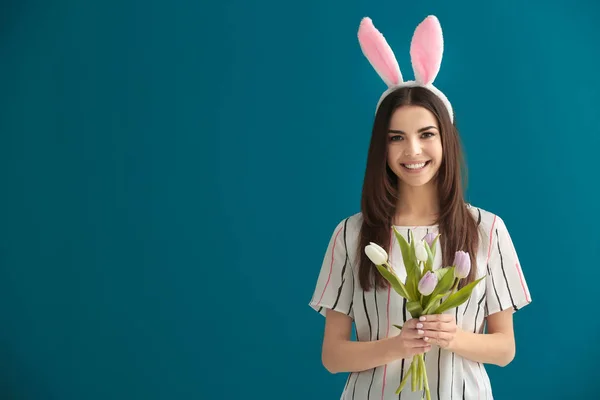 Vacker ung kvinna med Easter bunny öron och bukett blommor på färgbakgrund — Stockfoto
