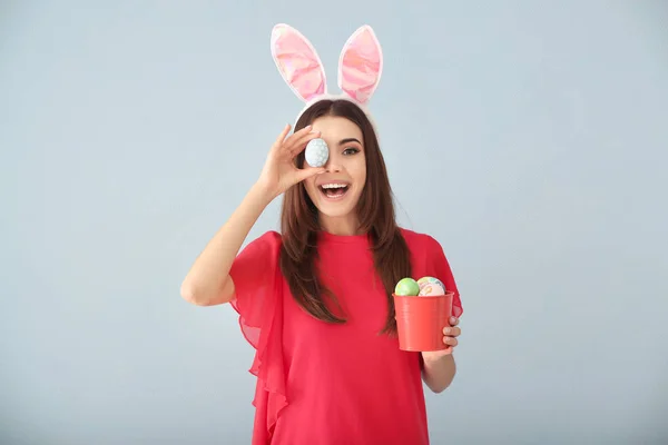 Mooie jonge vrouw met paaseieren en bunny oren op grijze achtergrond — Stockfoto