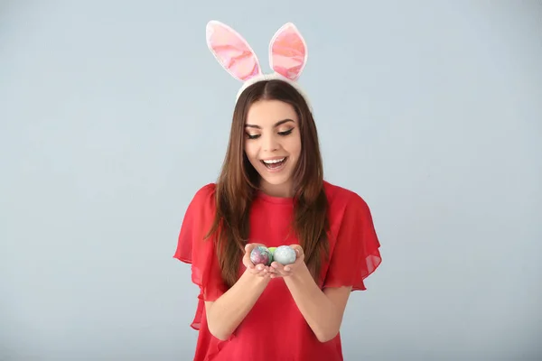 Krásná mladá žena s velikonoční vajíčka a uši zajíček na šedém pozadí — Stock fotografie