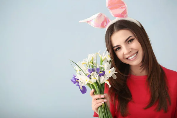 Vacker ung kvinna med Easter bunny öron och bukett blommor på grå bakgrund — Stockfoto