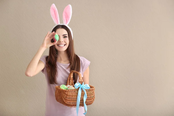 Schöne junge Frau mit Ostereiern und Hasenohren auf farbigem Hintergrund — Stockfoto