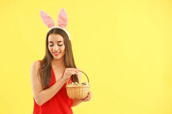 Bella giovane donna con uova di Pasqua e orecchie di coniglio su sfondo di colore — Foto Stock
