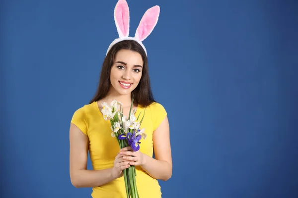 Красивая молодая женщина с пасхальными кроличьими ушами и букет цветов на цветном фоне — стоковое фото