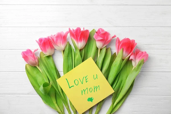 Hermosos tulipanes y tarjeta hecha a mano para el Día de la Madre sobre fondo de madera blanca, vista superior —  Fotos de Stock