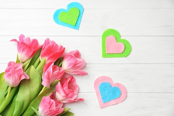 Hermosos tulipanes y corazones de fieltro decorativos sobre fondo de madera blanca — Foto de Stock