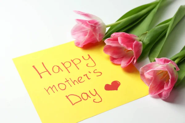 Hermosos tulipanes y tarjeta hecha a mano para el Día de la Madre sobre fondo blanco, primer plano — Foto de Stock