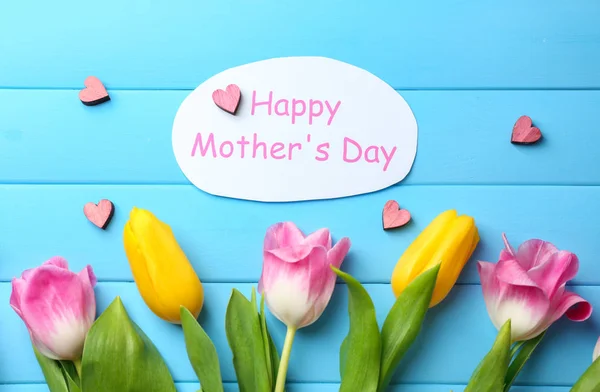 Tulipas bonitas e cartão feito à mão para o Dia das Mães na cor de fundo de madeira, vista superior — Fotografia de Stock