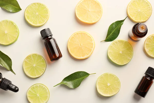 Bottles of essential oils and citrus slices on light background, top view — Stock Photo, Image