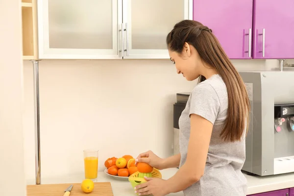 Hermosa joven mujer exprimiendo jugo de cítricos en la cocina —  Fotos de Stock