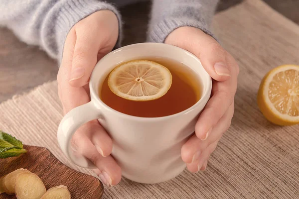 Mulher segurando xícara de chá de limão quente com gengibre na mesa — Fotografia de Stock
