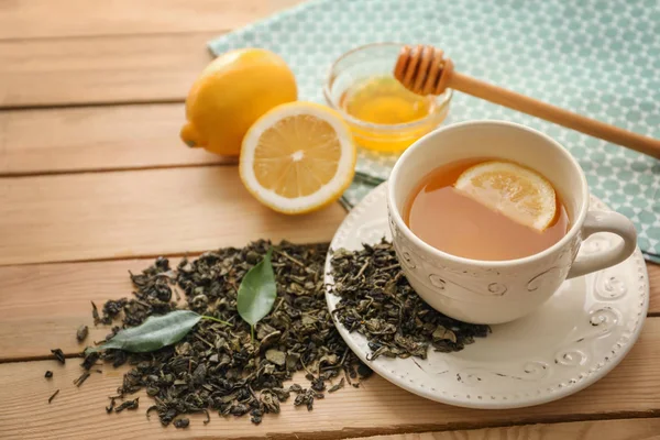 乾燥茶葉と木製のテーブルにレモン芳香族ドリンクのカップ — ストック写真