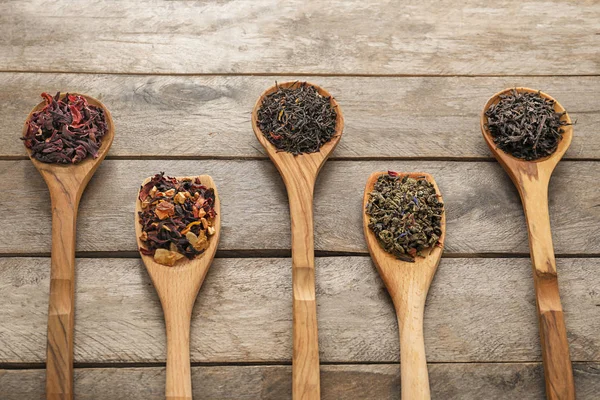 Lepels met verscheidenheid van droge thee bladeren op houten achtergrond — Stockfoto