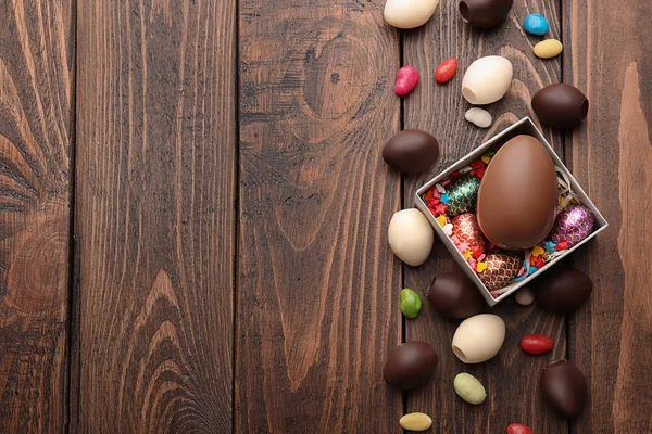 Ovos de Páscoa de chocolate com doces coloridos em fundo de madeira — Fotografia de Stock