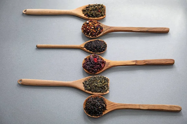 Lepels met verschillende soorten droge thee bladeren op grijze achtergrond — Stockfoto