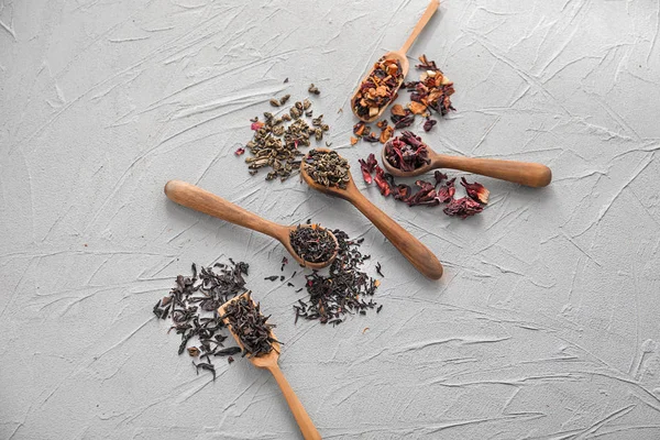Spoons with different types of dry tea leaves on light background — Stock Photo, Image