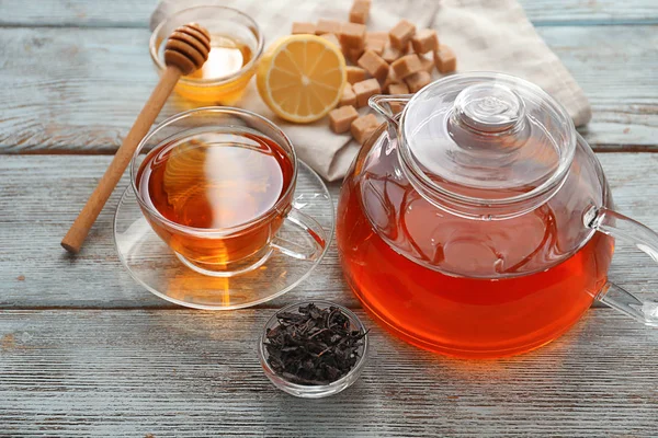 Hojas secas de té negro y tetera con taza de bebida aromática en la mesa — Foto de Stock