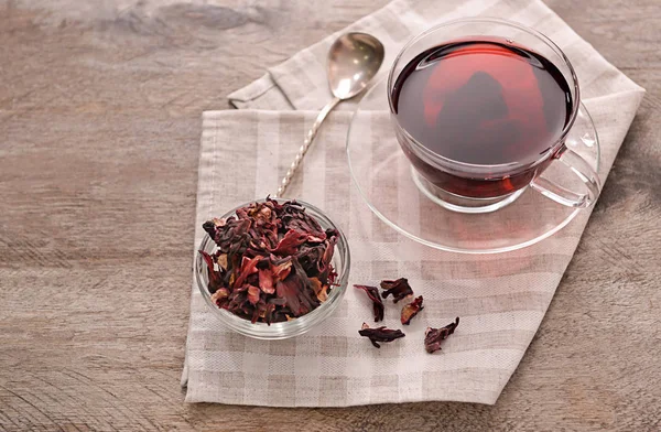 Bowl with dry hibiscus tea and cup of aromatic drink on wooden table