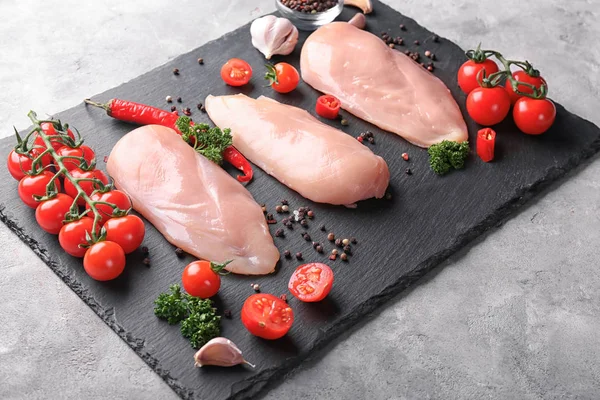 Raw chicken fillet with tomatoes and spices on slate plate