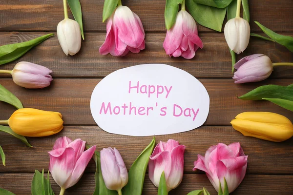 Krásné tulipány a ruční karta pro den matek na dřevěné pozadí, pohled shora — Stock fotografie