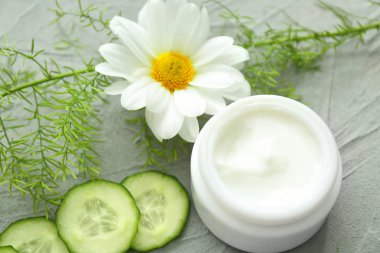 Bitkisel özü ve gri arka plan üzerine salatalık dilimleri ile krem kavanoz