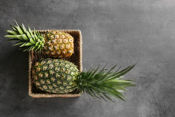 Wicker basket with fresh ripe pineapples on grey background — Stock Photo, Image