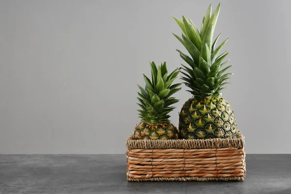 Wiklinowy kosz z dojrzałych ananasy na stole na szarym tle — Zdjęcie stockowe