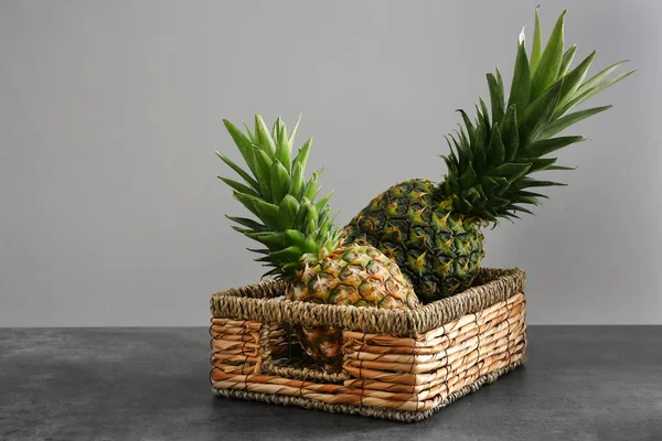 Wicker basket with fresh ripe pineapples on table against grey background — Stock Photo, Image