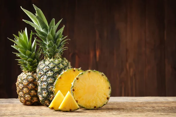 Whole and cut ripe pineapples on wooden table — Stock Photo, Image
