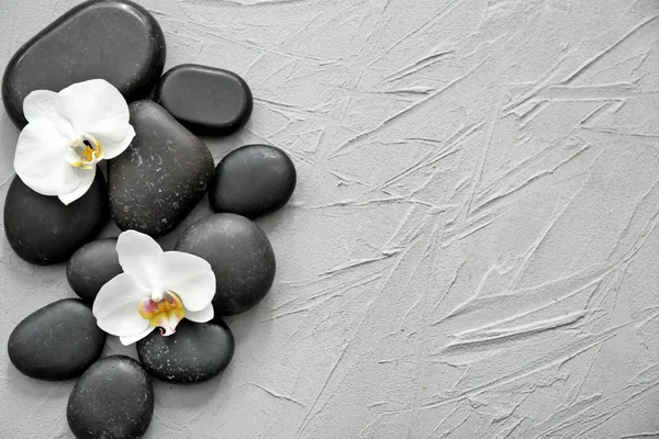 Kamienie spa i piękne kwiaty orchidei na szary teksturowanej tło — Zdjęcie stockowe