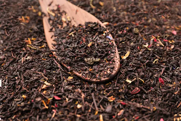 Dry black tea leaves with flower petals and spoon on table — Stock Photo, Image