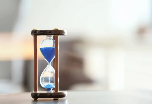 Hourglass di atas meja terhadap latar belakang kabur. Konsep manajemen waktu — Stok Foto