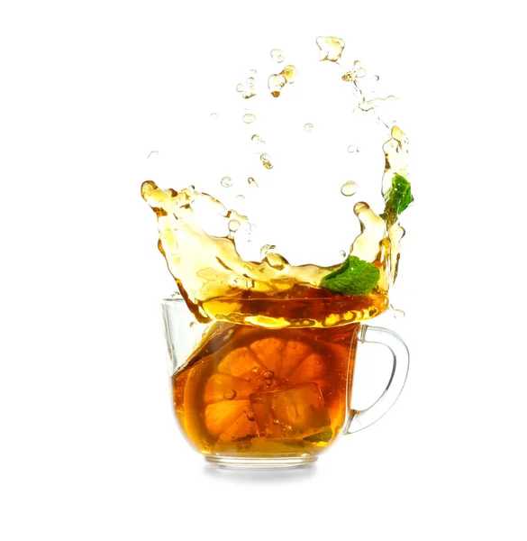 Copa de vidrio y salpicadura de delicioso té de limón con jengibre sobre fondo blanco — Foto de Stock