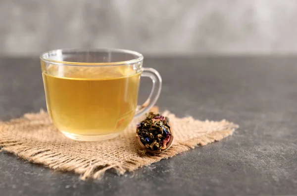 Dried green tea leaves and cup of aromatic drink on table — Stock Photo, Image