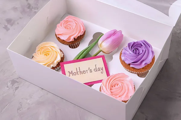 Box with tasty cupcakes and tulip on grey background. Mother's day celebration — Stock Photo, Image