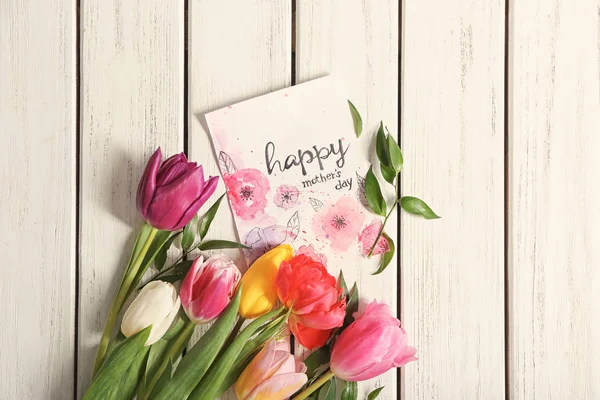 Kort med ord glad mors dag och blommor på trä bakgrund, ovanifrån — Stockfoto