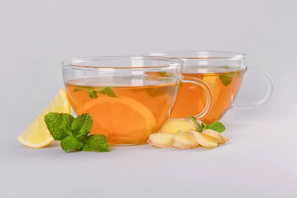 Cups of hot lemon tea with ginger on grey background — Stock Photo, Image