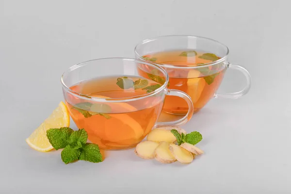 Cups of hot lemon tea with ginger on grey background — Stock Photo, Image