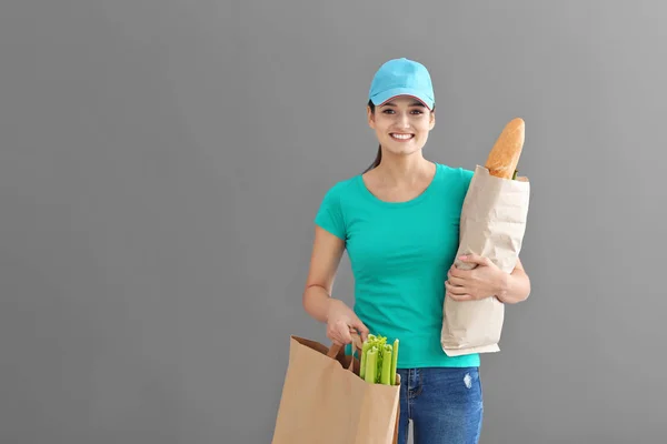 Delivery woman holding paper bags with food on grey background — Stock Photo, Image