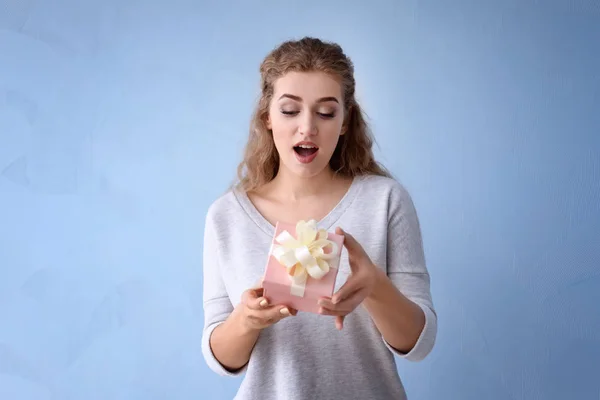 Mooie jonge vrouw met cadeau doos op kleur achtergrond — Stockfoto