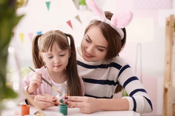 Mother painting Easter eggs with her daughter at table — Stock Photo, Image