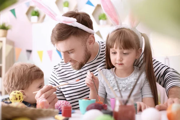 Отец рисует пасхальные яйца со своими детьми за столом — стоковое фото