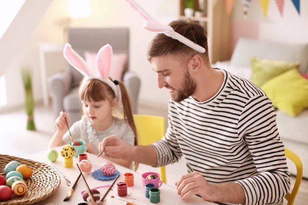 Father painting Easter eggs with his daughter at table